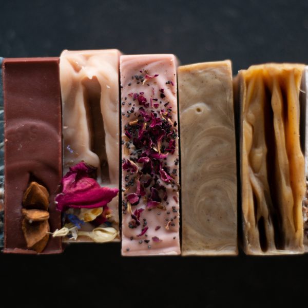 A dark background with a row of 5 handmade soaps in various colours and textures