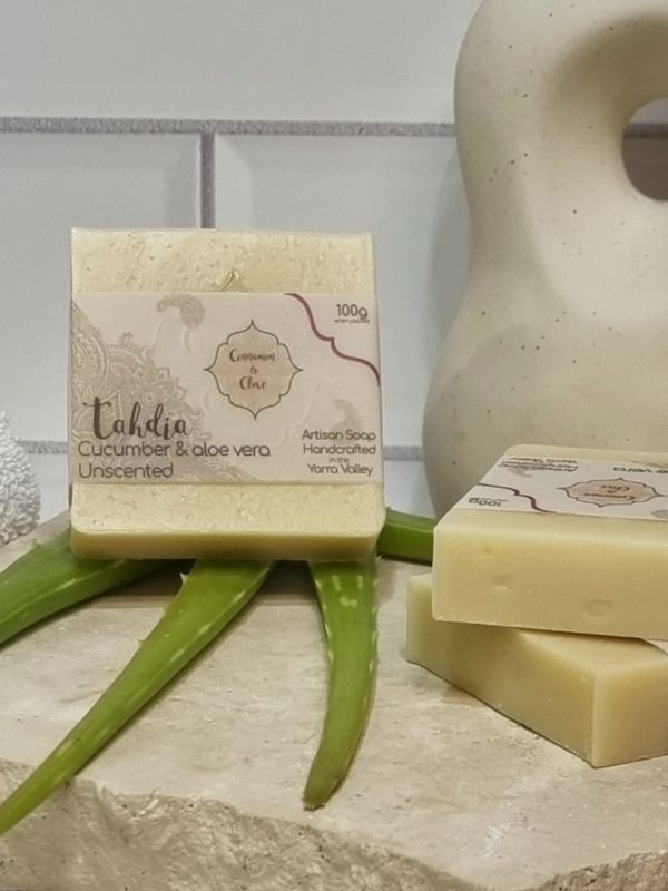 A tile background and a piece of terrazzo. Three bars of creamy coloured homemade soap are sitting on the terrazo, with fresh aloe vera to decorate. Also in the background is and a curvy decorative statue